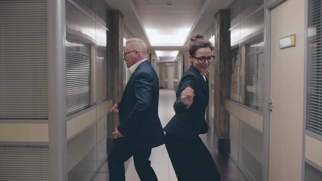 Funny businesswoman and businessman dancing in office corridor celebrating success of project and victory of teamwork. Motivational corporate shot