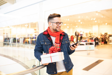 Charming hipster guy smiling and chatting on his smart-phone. He is wearing glasses and a scarf. He...