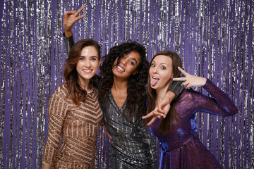 Beautiful cheerful women in fancy sparkling dresses posing isolated over vibrant purple violet silver background. Positive people spending time on happy birthday new year holiday party discotheque.