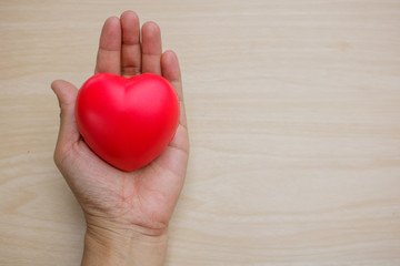 Red heart on hand on wooden background.