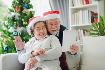 Senior Asian couple family celebration in Christmas day, Retired man and woman using tablet to video call with young family smile felling happy in living room at home. Merry Xmas and happy new year.