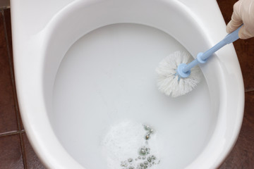 Female hands in gloves wash and disinfect a white toilet with a brush and cleaning agent