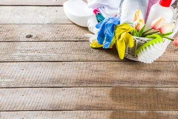 Spring home cleaning and housekeeping concept, Basket with cleaning items, utensils, supplies. Copy space over wooden background with spring blossom flowers
