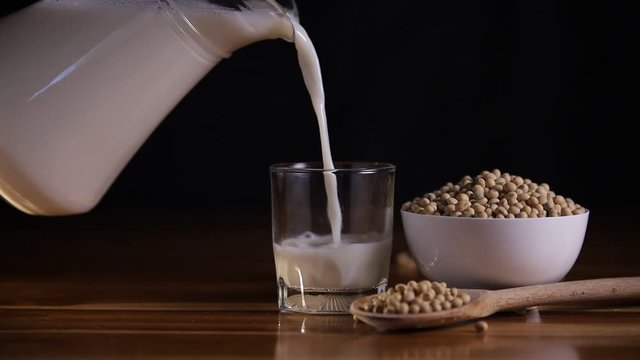 Pouring soy milk into glass on wooden table background on table have soybeans in cup, spoon wooden and soy milk pitcher.