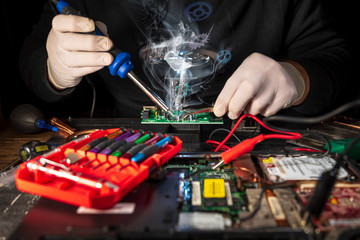 Hands of a man in white gloves repair laptop using soldering iron