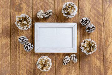 Photo frame between Christmas decoration, with pine cones on a brown wooden table. Top view, frame to copy space