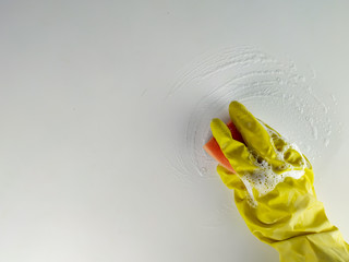 Top view of a hand in a yellow rubber glove with sponge rubbing the detergent and spreading foam on a white background as a concept of domestic cleaning