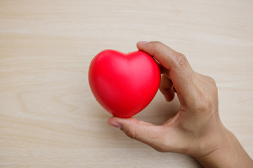 Red heart on hand on wooden background.