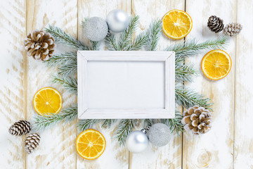 Photo frame between Christmas decoration, with white balls and pine cones on a white wooden table. Top view, frame to copy space