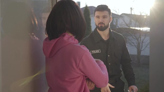 Young bearded Caucasian detective standing in sunrays with documents, talking to brunette woman, and shaking her hand. Handsome detective investigating crime. Testimony, interrogation.