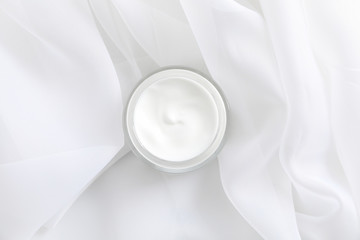 Jar of winter cream for skin on white fabric background, top view. Space for text