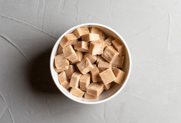 Refined cane sugar in a white bowl on a grey table, top view.