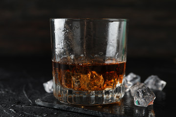 Glass of whiskey and ice cubes on black background, close up