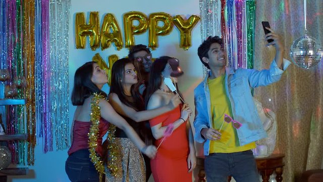Indian boys and girls happily posing with photo props during New Year time - party concept. Group of happy young friends having fun while clicking selfies in a party photo booth - New Year celebrat...