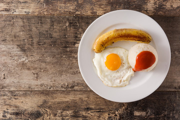 Arroz a la cubana Typical Cuban rice with fried banana and fried egg on a plate on wooden table. Top view. Copy space	