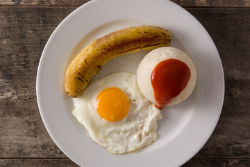 Arroz a la cubana Typical Cuban rice with fried banana and fried egg on a plate on wooden table. Top view. 