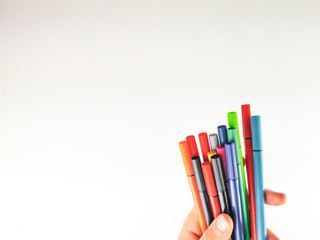 Closeup and side view of a hand holding many pens in different colors on white background as blank canvas for expressing imagination and for school