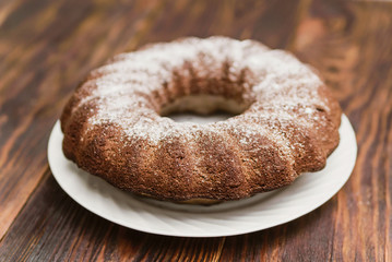 round chocolate cake sprinkled with powdered sugar on a wooden background