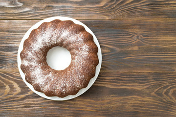 round chocolate cake sprinkled with powdered sugar on a wooden background