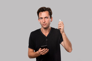 Young handsome man with wireless earbuds holding smartphone.