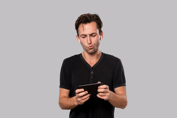 Young handsome man with wireless earbuds holding smartphone.