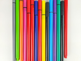 Closeup of many colorful pens with caps and vivid colors lined randomly on white background used by students and kids for note taking and coloring