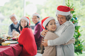 Big Asian family celebration in Christmas day, grandmother hug and looking at granddaughter in front of meal table of family which smiling and felling happy at home. Merry Xmas and happy new year.