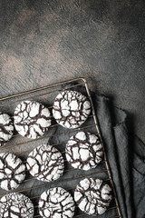 Chocolate crinkle cookies with powdered sugar icing. Cracked chocolate biscuits on an iron lattice on a dark background top view copy space