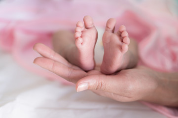 Obraz na płótnie Canvas Baby foots on mother hand.Newborn baby feet and relax action with pink blanket.Happy time family concept.