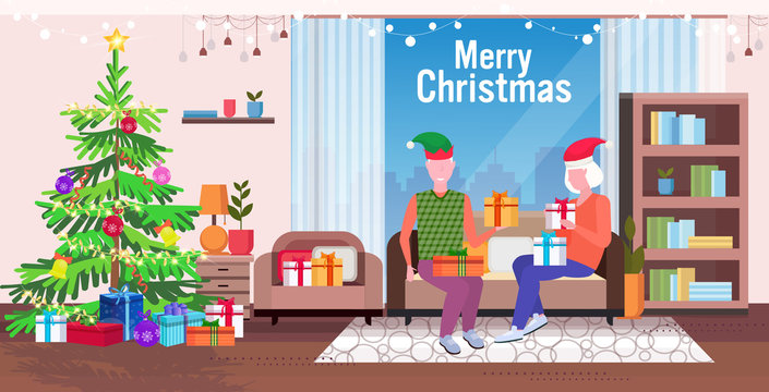 senior man in elf hat giving present gift box to mature woman family sitting on couch celebrating merry christmas happy new year winter holidays concept modern living room interior full length