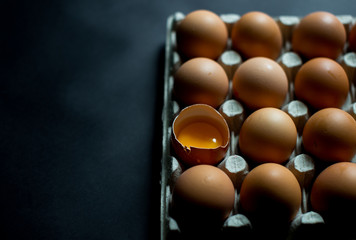 A dozen eggs in a cardboard open package on a black background top view. Fresh broken quail eggs lies in a cardboard box (a beautiful yellow yolks in the shell). Copy space. Abstract concept