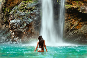 Fototapeta na wymiar Young slim brunette woman with curly hair enjoying in lagoon of huge tropical waterfall Banyumala in Bali. Wearing in black swimsuit. Happy vacations in Indonesia. Wanderlust travel concept.