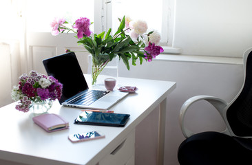 Female office desk workspace homeoffice mock up with laptop, pink peony flowers bouquet, smartphone, pink accessories and pink cup of coffee. Fashion, beauty or lifestyle blog concept.