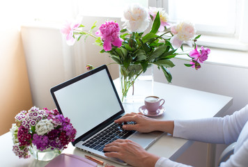 Female hands using laptop. Female office desk workspace homeoffice mock up with laptop, pink peony flowers bouquet, smartphone, pink accessories and pink cup of coffee.