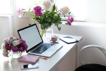 Female office desk workspace homeoffice mock up with laptop, pink peony flowers bouquet, smartphone, pink accessories and pink cup of coffee. Fashion, beauty or lifestyle blog concept.