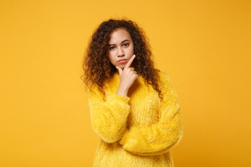 Pensive young african american girl in fur sweater posing isolated on yellow orange background studio portrait. People sincere emotions lifestyle concept. Mock up copy space. Put hand prop up on chin.