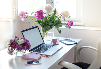 Female office desk workspace homeoffice mock up with laptop, pink peony flowers bouquet, smartphone, pink accessories and pink cup of coffee. Fashion, beauty or lifestyle blog concept.