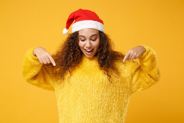 Excited young african american Santa girl in fur sweater, Christmas hat isolated on yellow...