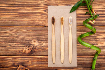 Bamboo toothbrushes, bamboo branch on wooden background. Flat lay copy space. Natural bath...