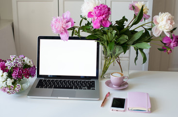 Female office desk workspace homeoffice mock up with laptop, pink peony flowers bouquet, smartphone, pink accessories and pink cup of coffee. Fashion, beauty or lifestyle blog concept.