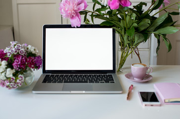 Female office desk workspace homeoffice mock up with laptop, pink peony flowers bouquet, smartphone, pink accessories and pink cup of coffee. Fashion, beauty or lifestyle blog concept.