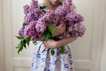 Blonde hair woman in dress posing with bouquet of lilac flowers over white background. Lilac flower in a female hands.