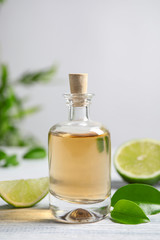 Lime essential oil and cut citrus fruits on white wooden table