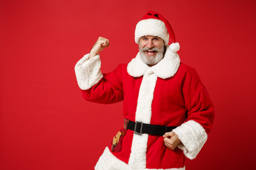 Fototapeta na wymiar Happy elderly gray-haired mustache bearded Santa man in Christmas hat posing isolated on red background. New Year 2020 celebration holiday concept. Mock up copy space. Clenching fists like winner.