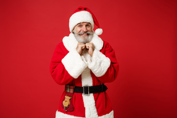 Smiling elderly gray-haired mustache bearded Santa man in Christmas hat posing isolated on red wall background. Happy New Year 2020 celebration holiday concept. Mock up copy space. Clenching fists.