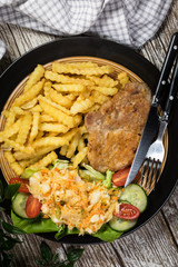 Fried pork chop in breadcrumbs, served with fries and salad.