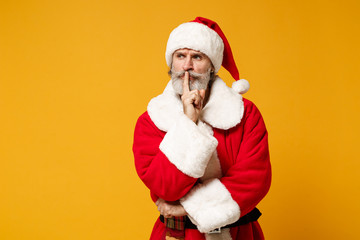 Fototapeta na wymiar Elderly gray-haired mustache bearded Santa man in Christmas hat posing isolated on yellow background. New Year 2020 celebration concept. Mock up copy space. Say hush with finger on lips shhh gesture.