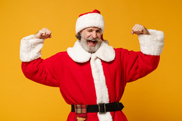 Fototapeta na wymiar Funny elderly gray-haired mustache bearded Santa man in Christmas hat posing isolated on yellow wall background. Happy New Year 2020 celebration concept. Mock up copy space. Showing biceps, muscles.