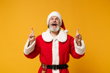 Excited elderly gray-haired bearded mustache Santa man in Christmas hat posing isolated on yellow...
