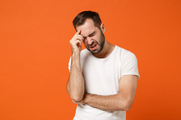 Displeased young man in casual white t-shirt posing isolated on orange wall background, studio...